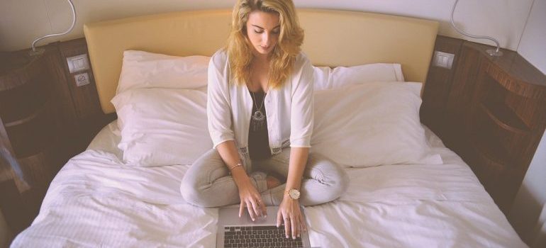 A woman sitting on a bed, working on a laptop.