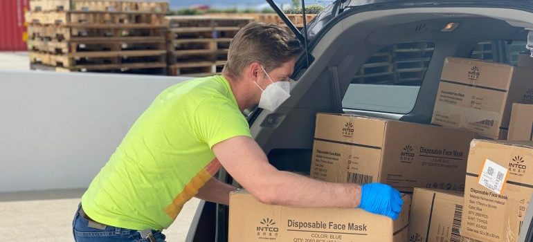 A man with gloves and face masks storing boxes in a vehicle.