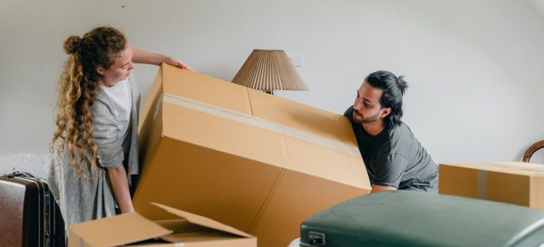 Woman and man carrying moving cardboard box in the apartment.