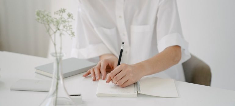 a woman in a white shirt writing down her plans in a notebook